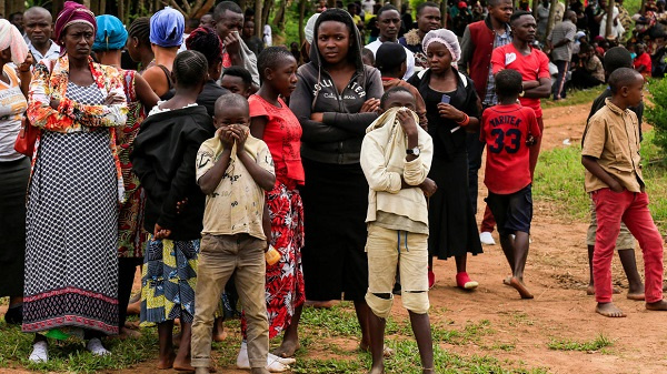 Scores of people gather at the scene where 14 bodies were found hacked to death